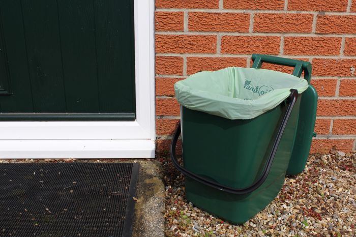 Green outdoor caddy with a 30L BioLiner compostable bag placed beside a brick wall