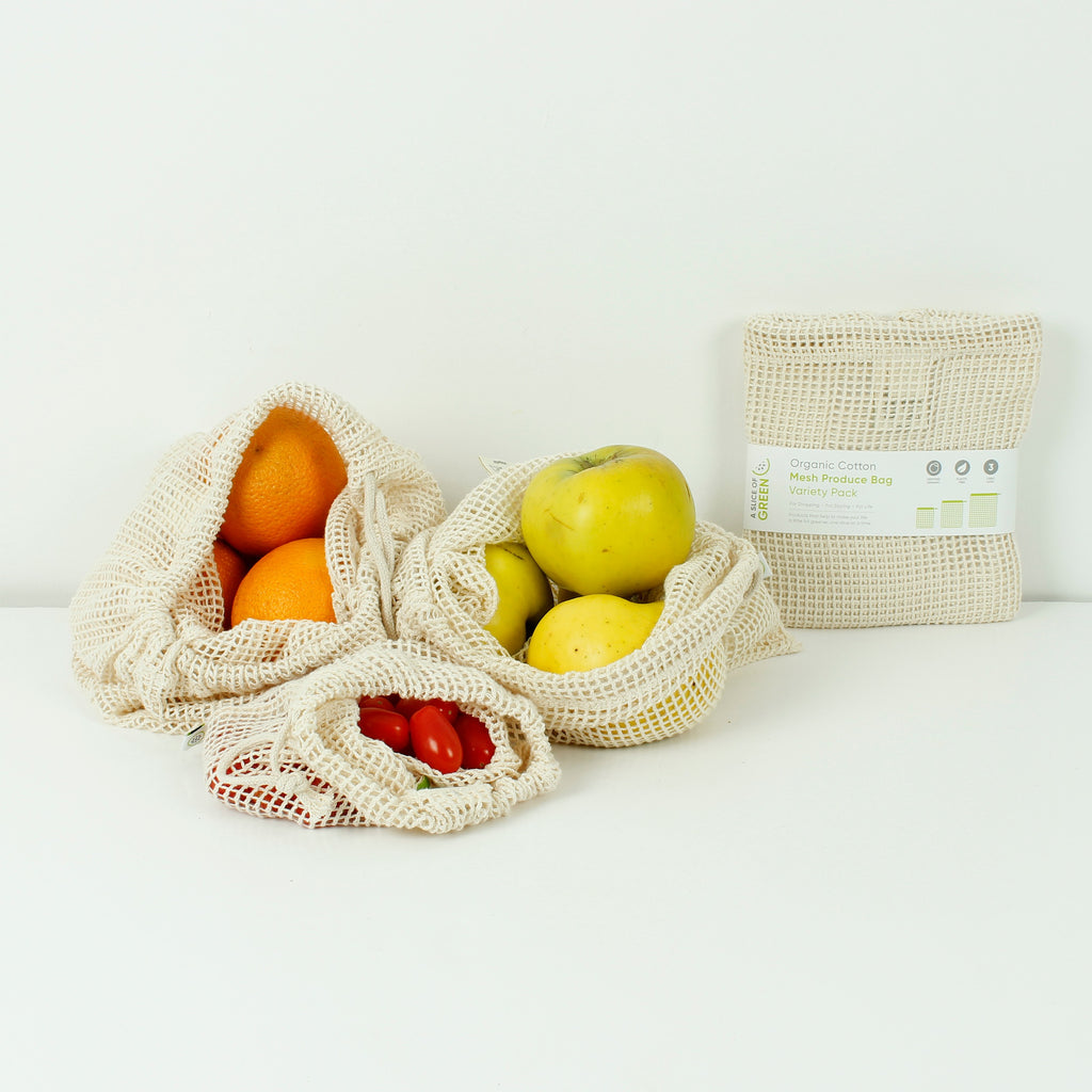Organic cotton mesh produce bags filled with oranges, apples and cherry tomatoes on white background