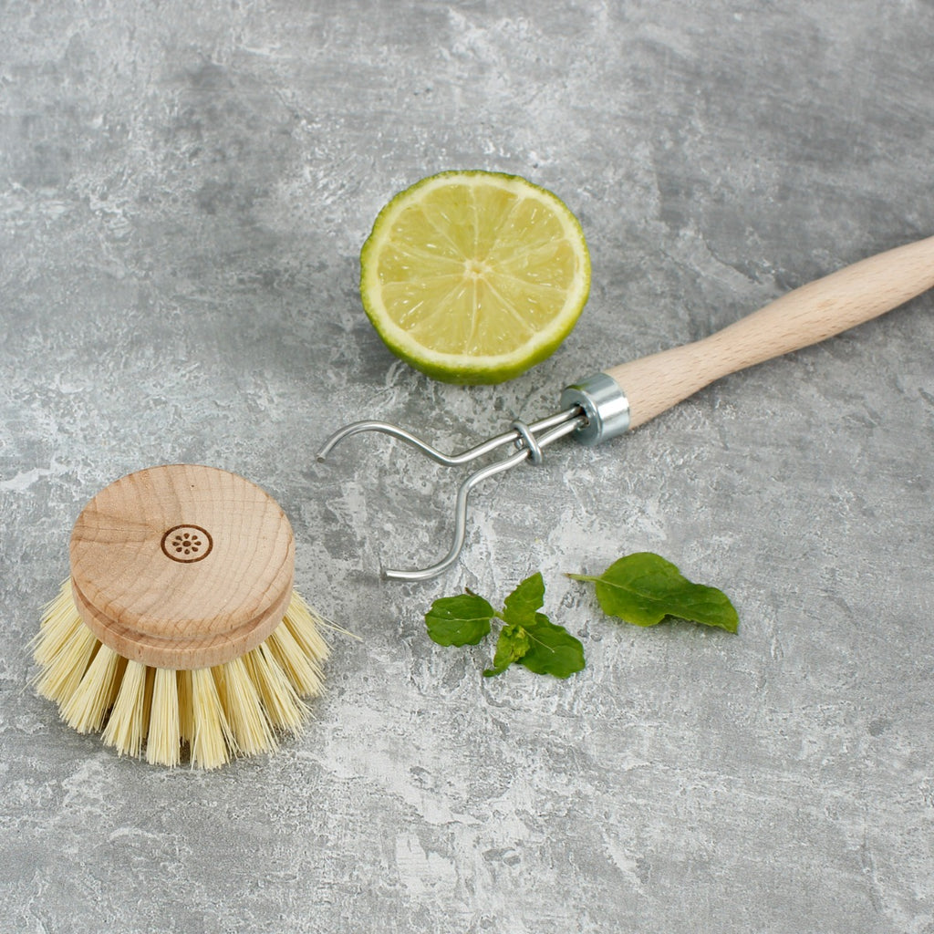 Wooden scrub brush with round head and kitchen hook on grey surface with mint leaves and lime slice