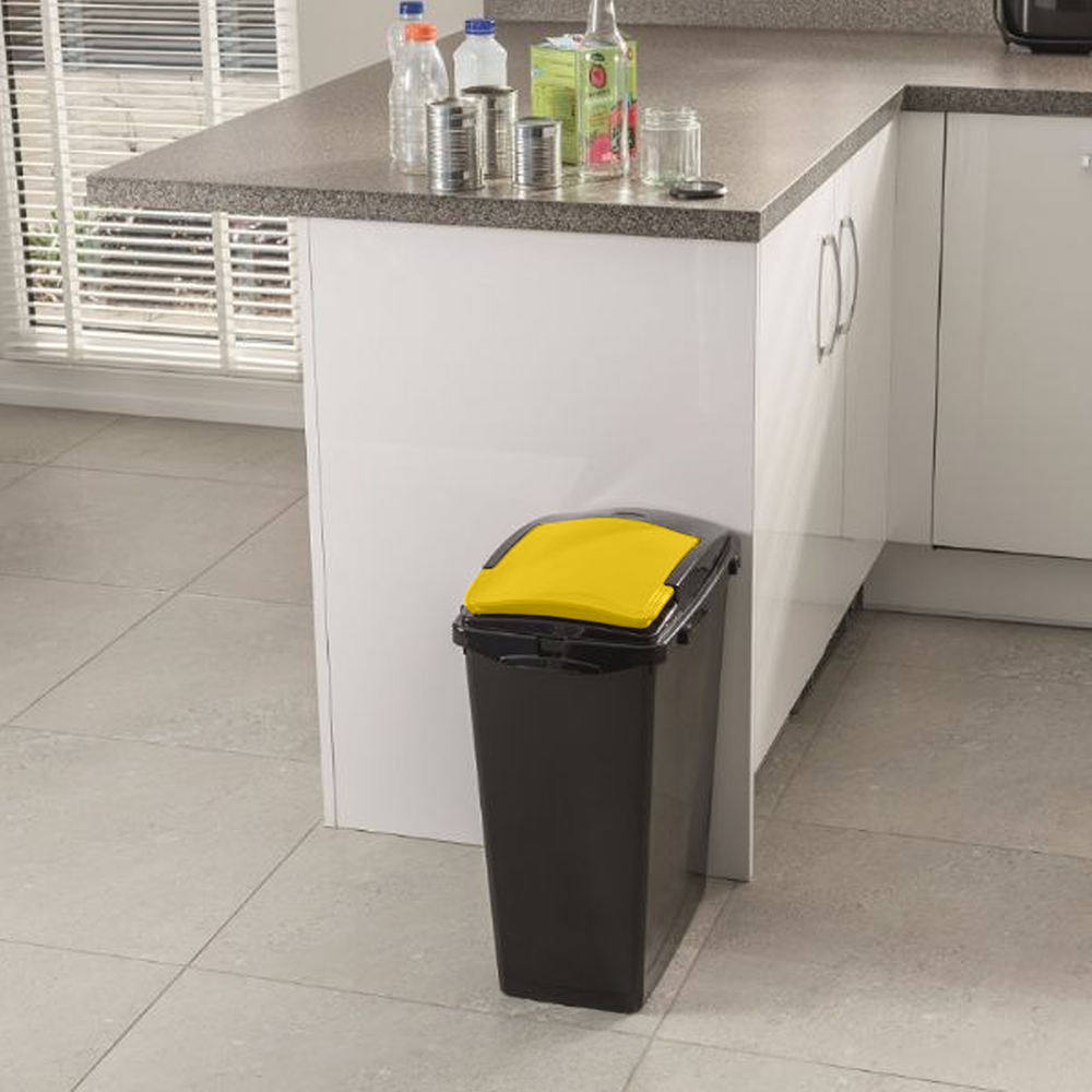 Slim black bin with yellow lid placed in a modern kitchen corner, next to food waste items.
