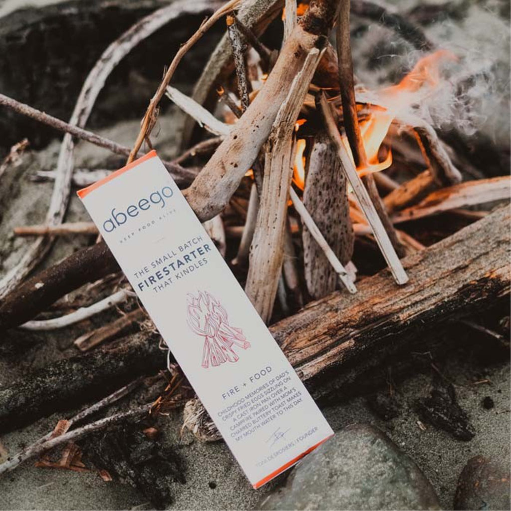 Abeego firestarter pack leaning on lit kindling with small flames and smoke in a natural outdoor setting
