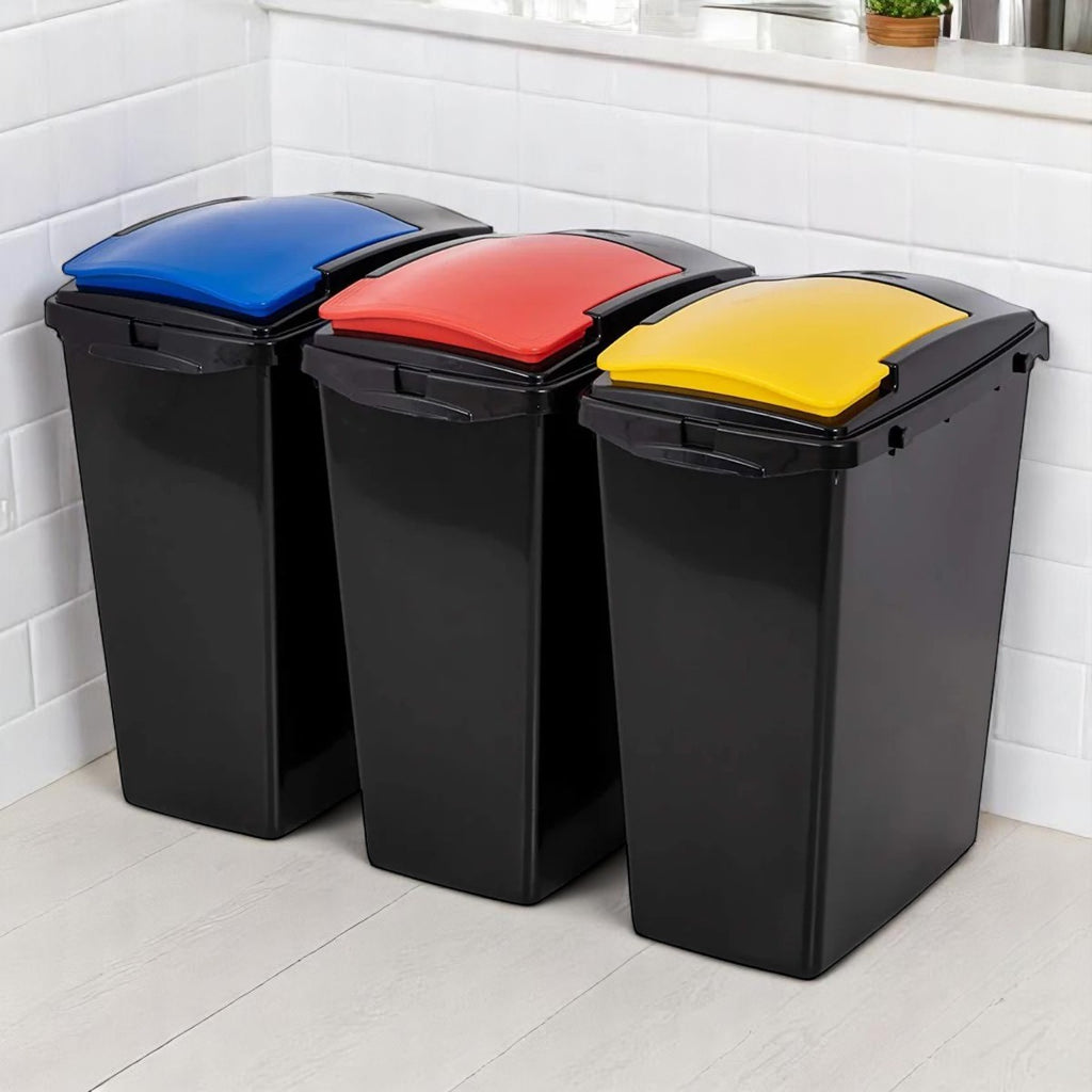 Three black kitchen recycling bins with blue, red and yellow lids, lined up against a white tiled wall for organised waste sorting.