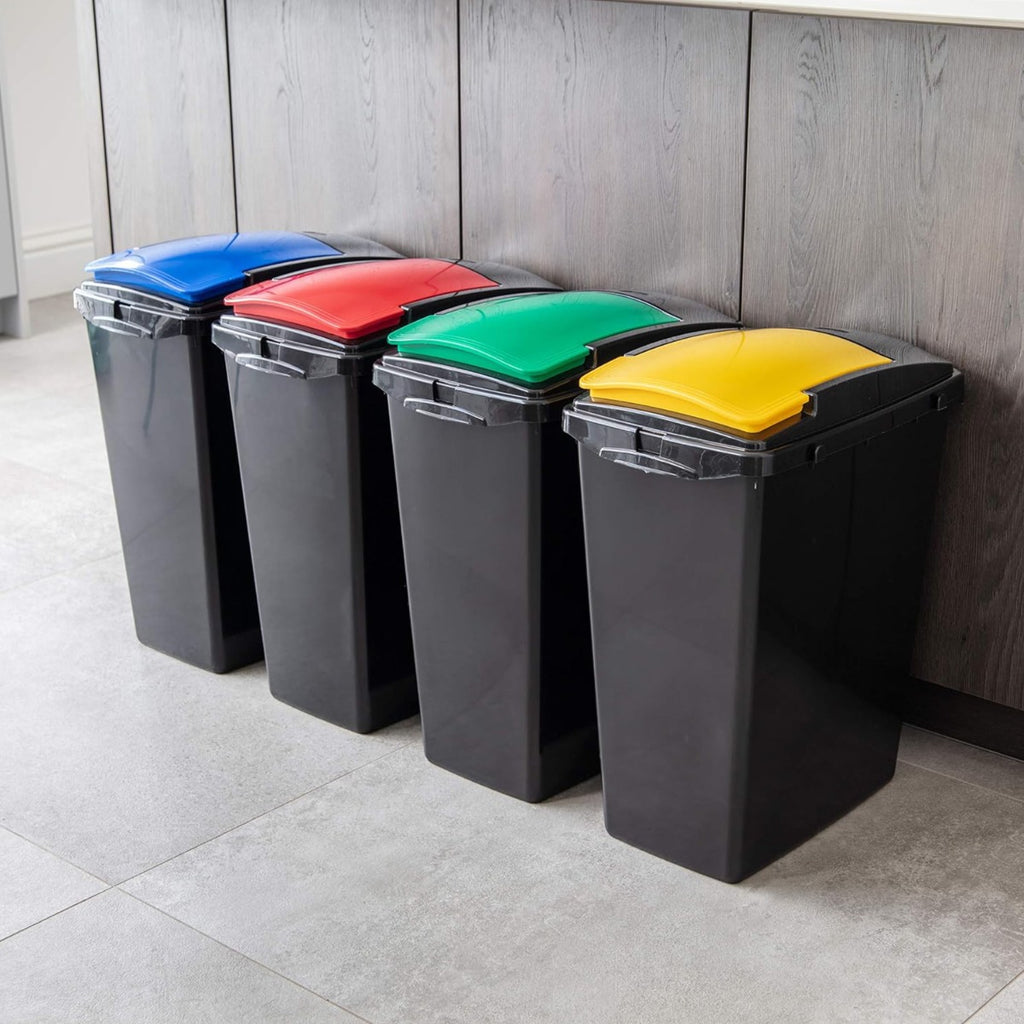 Four black recycling bins with blue, red, green, and yellow lids lined up in a modern kitchen against dark wood cabinets.