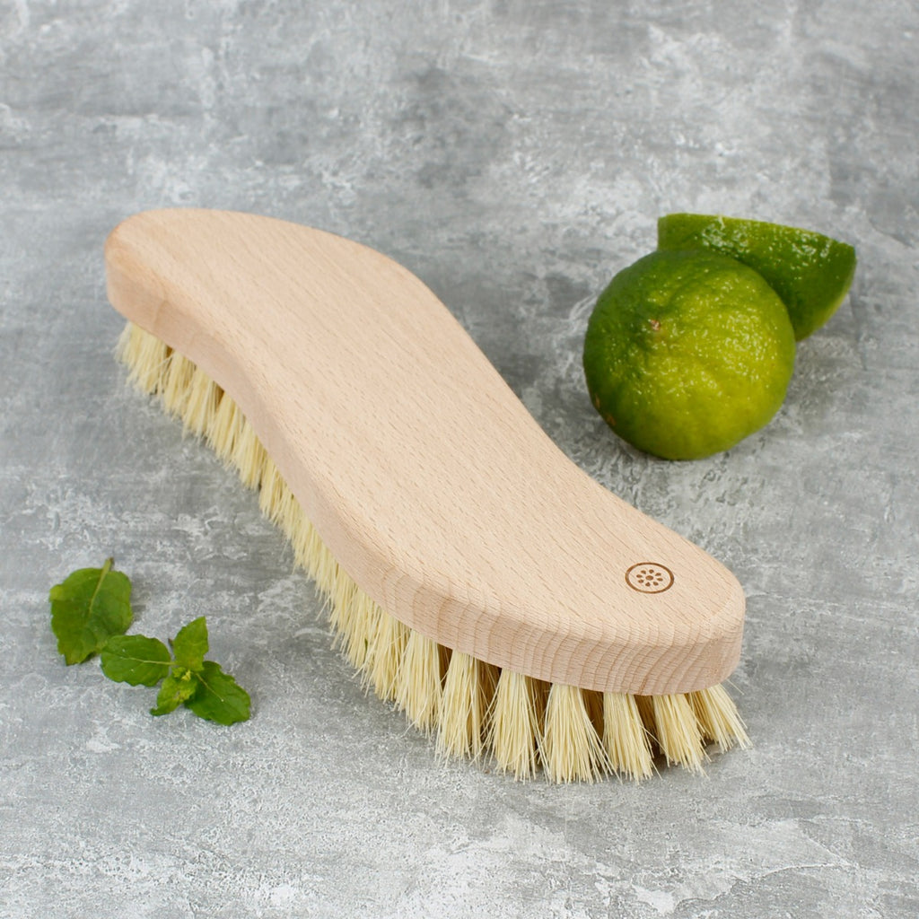 Curved wooden scrubbing brush with natural bristles on stone surface beside fresh lime and mint leaves