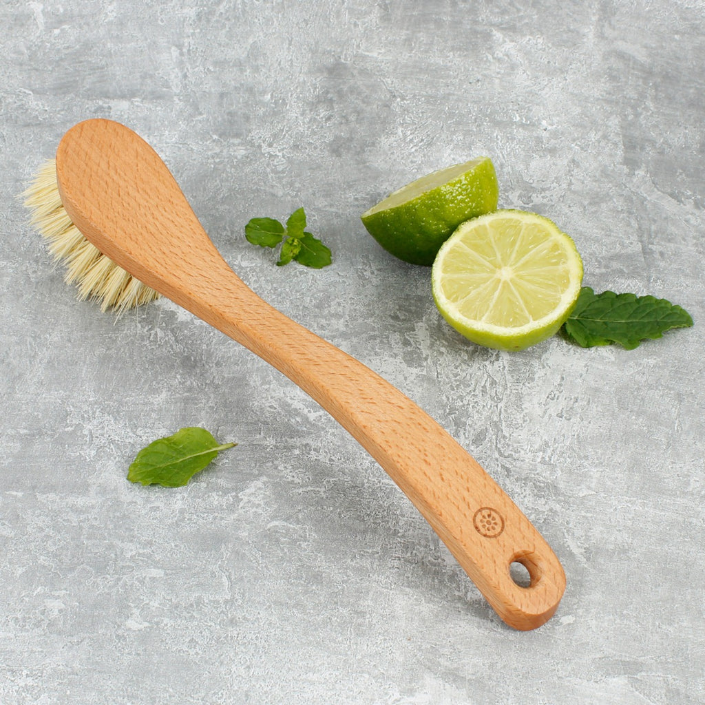 Wooden dish brush with light bristles on stone surface beside sliced lime and fresh mint leaves