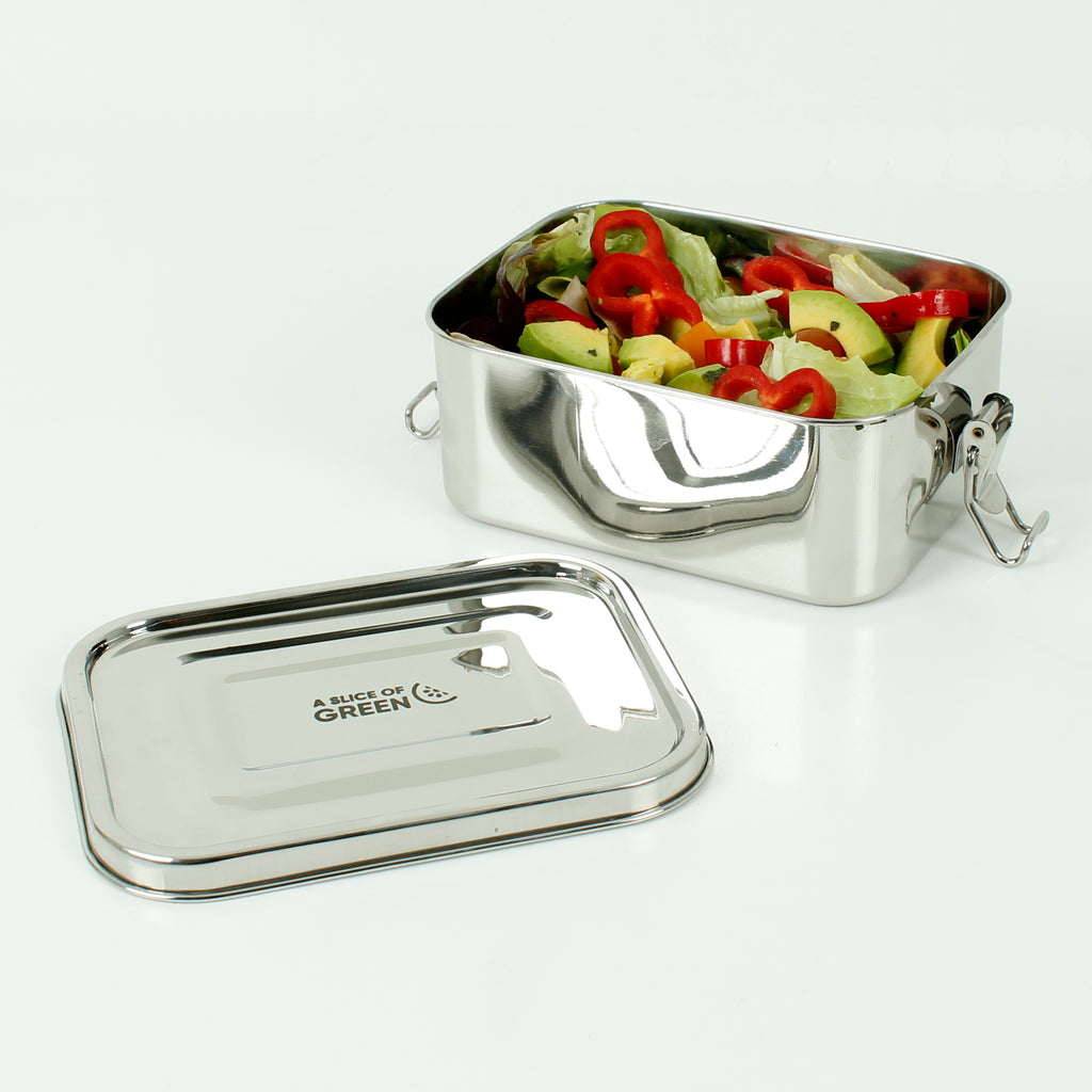 Open stainless steel lunch box filled with fresh salad, red peppers and avocado, with lid placed beside it on a white surface