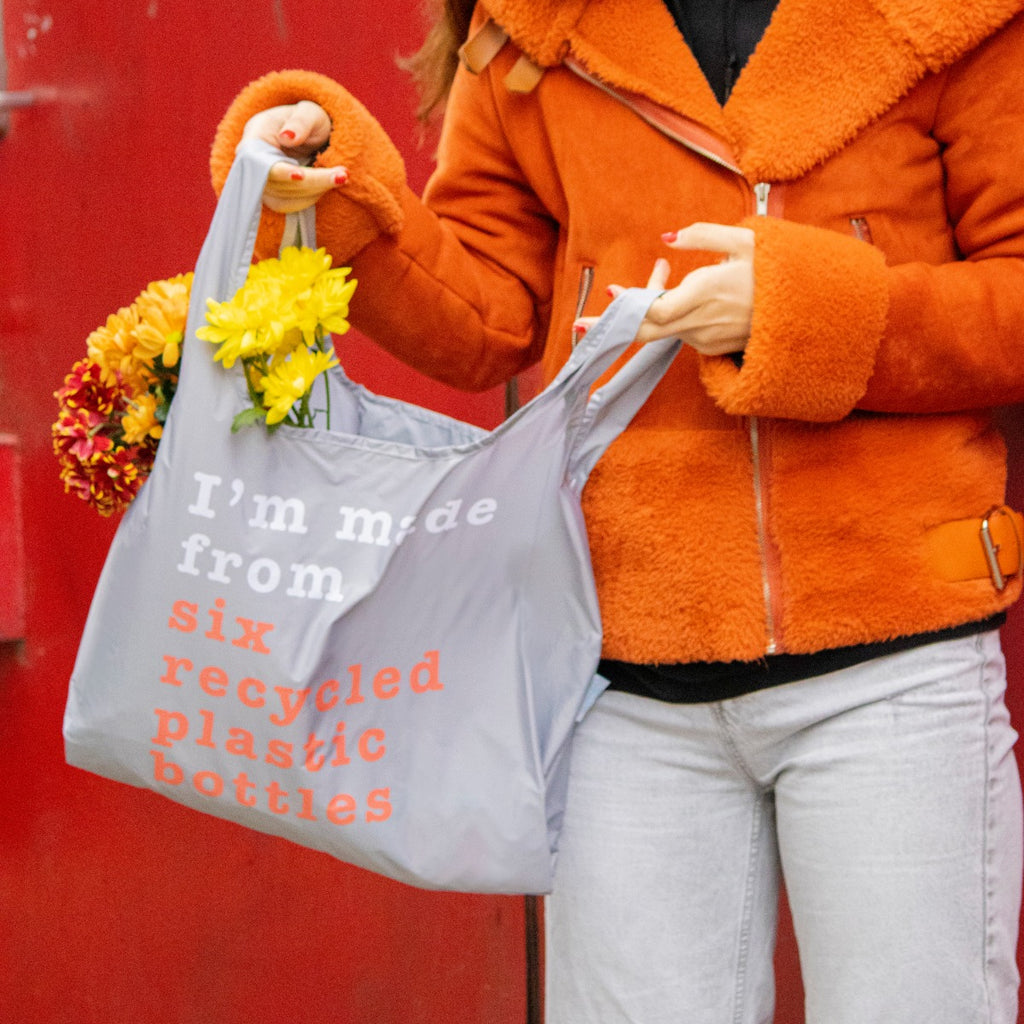 Person holding grey and coral shopping bag full of flowers