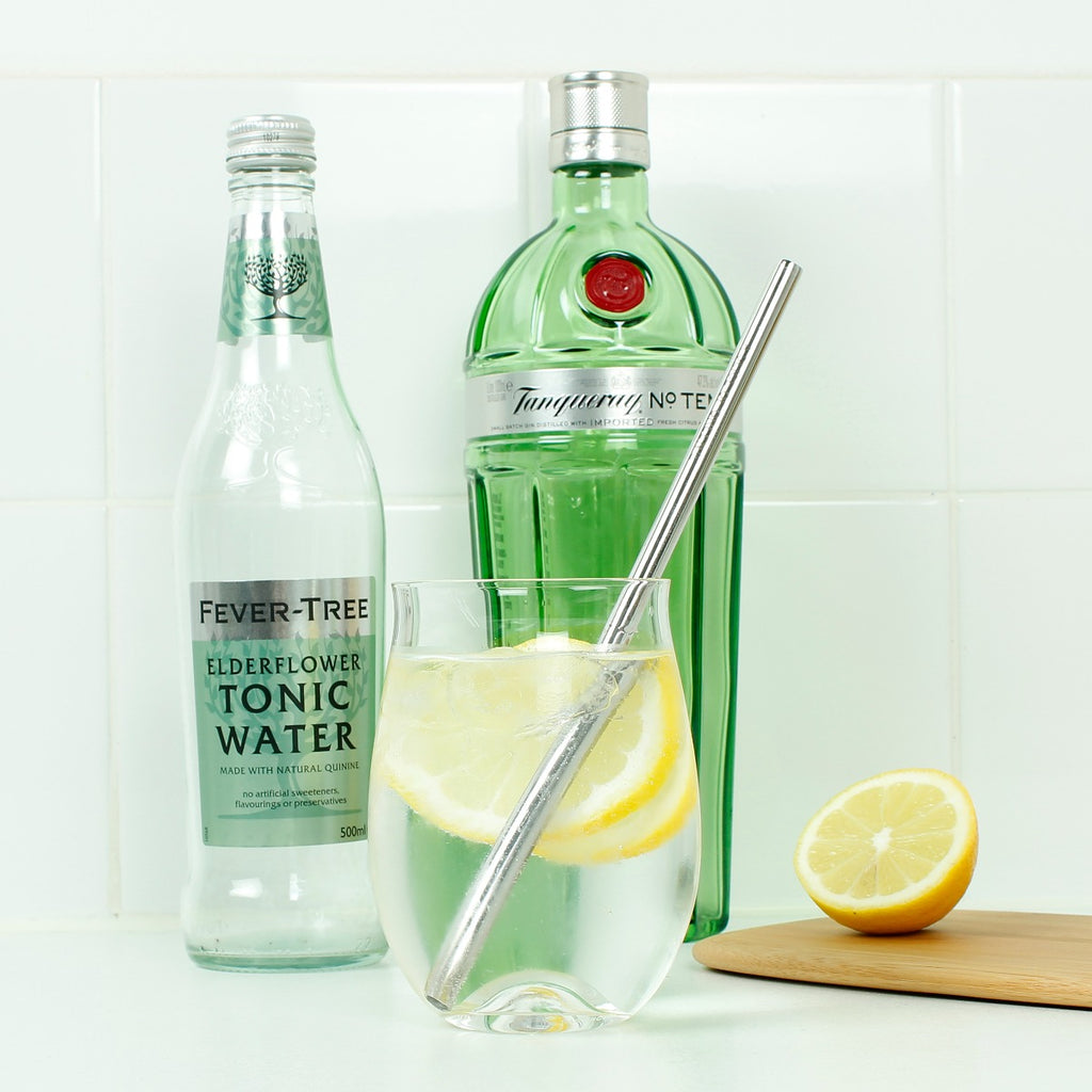 Stainless steel straw in a glass of lemon gin and tonic, with Fever-Tree tonic and Tanqueray gin bottles in a kitchen setting