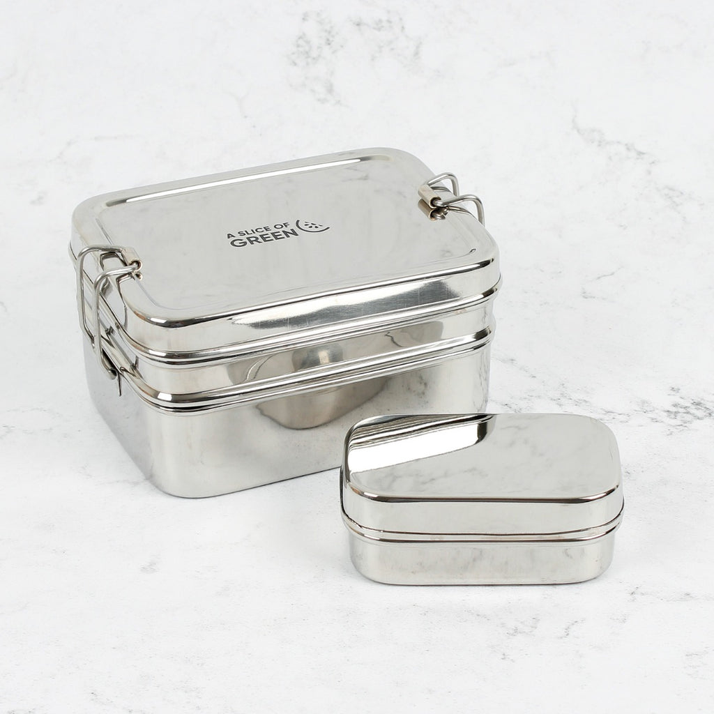 Two stacked stainless steel lunch boxes, one large with clips and one small, both with a polished finish on a white marble surface