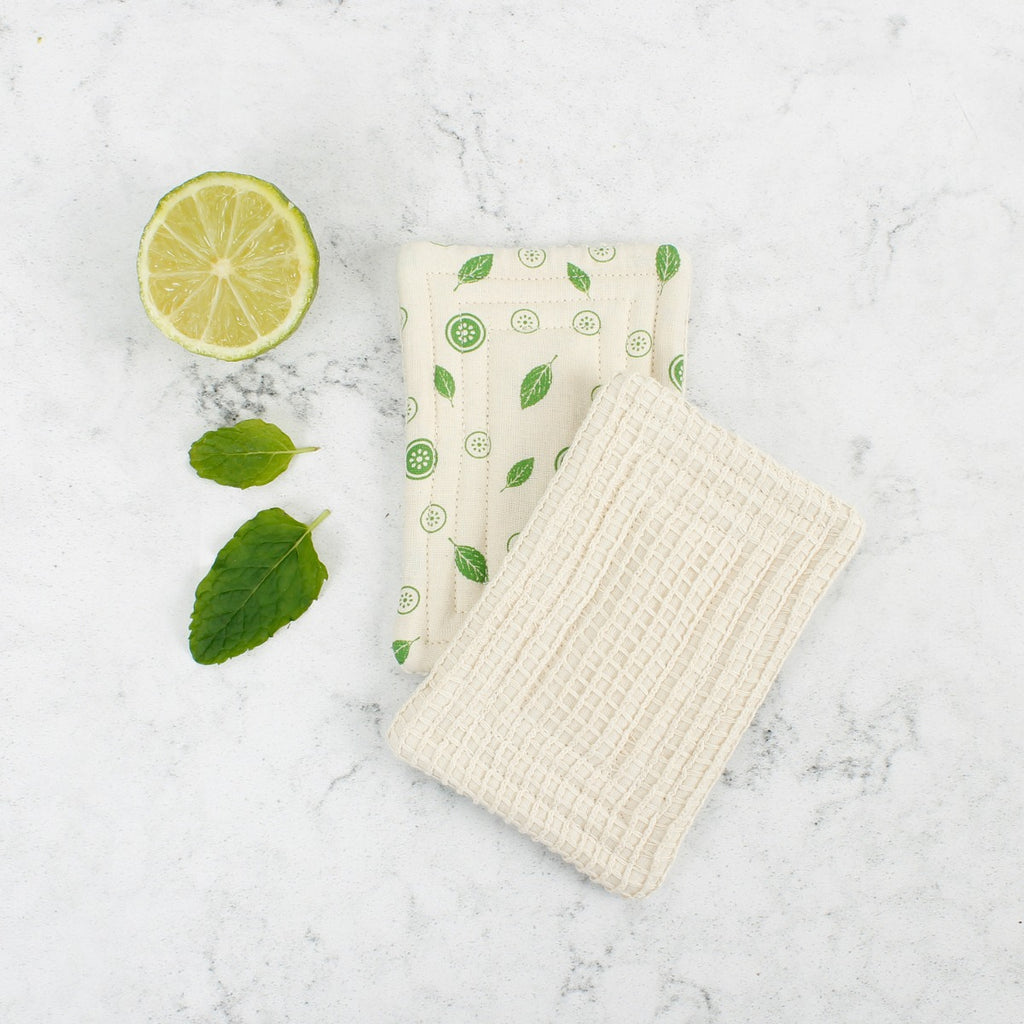 Two sides of a mint leaf Scrub Unsponge, one waffle-textured and one smooth, shown on marble with mint and lime