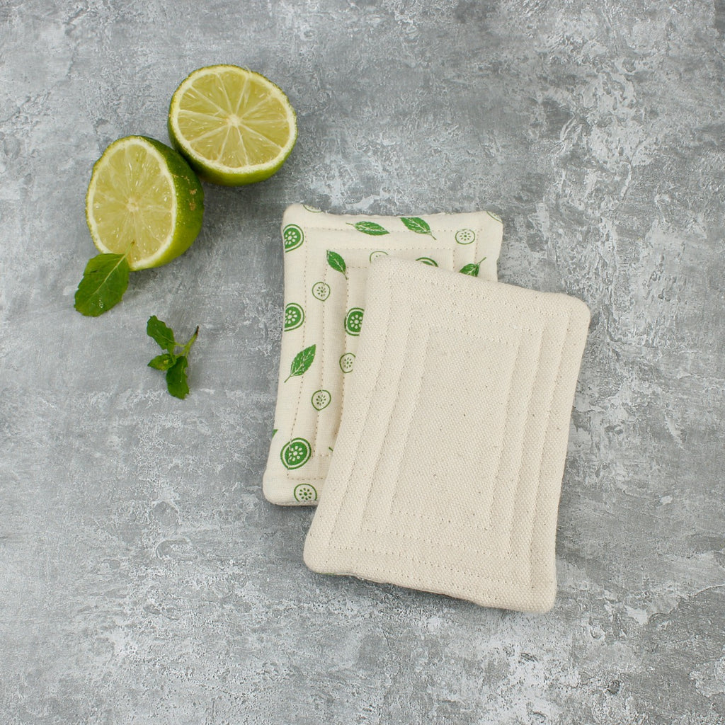 Two organic cotton Smooth Unsponges, one plain and one printed, on grey surface with lime slices and mint
