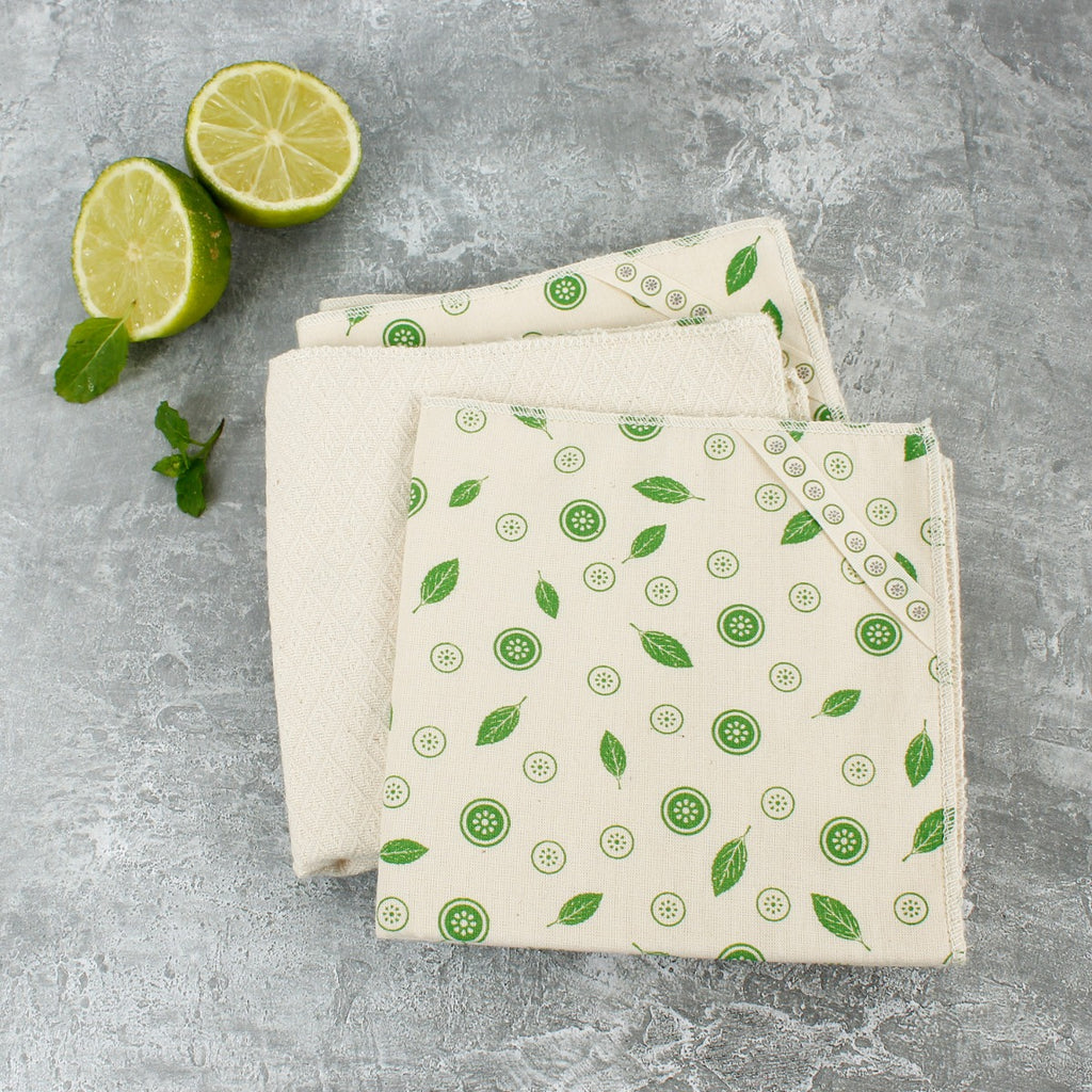 Folded organic cotton unpaper towels with green mint leaf print on grey surface beside lime slices and mint leaves