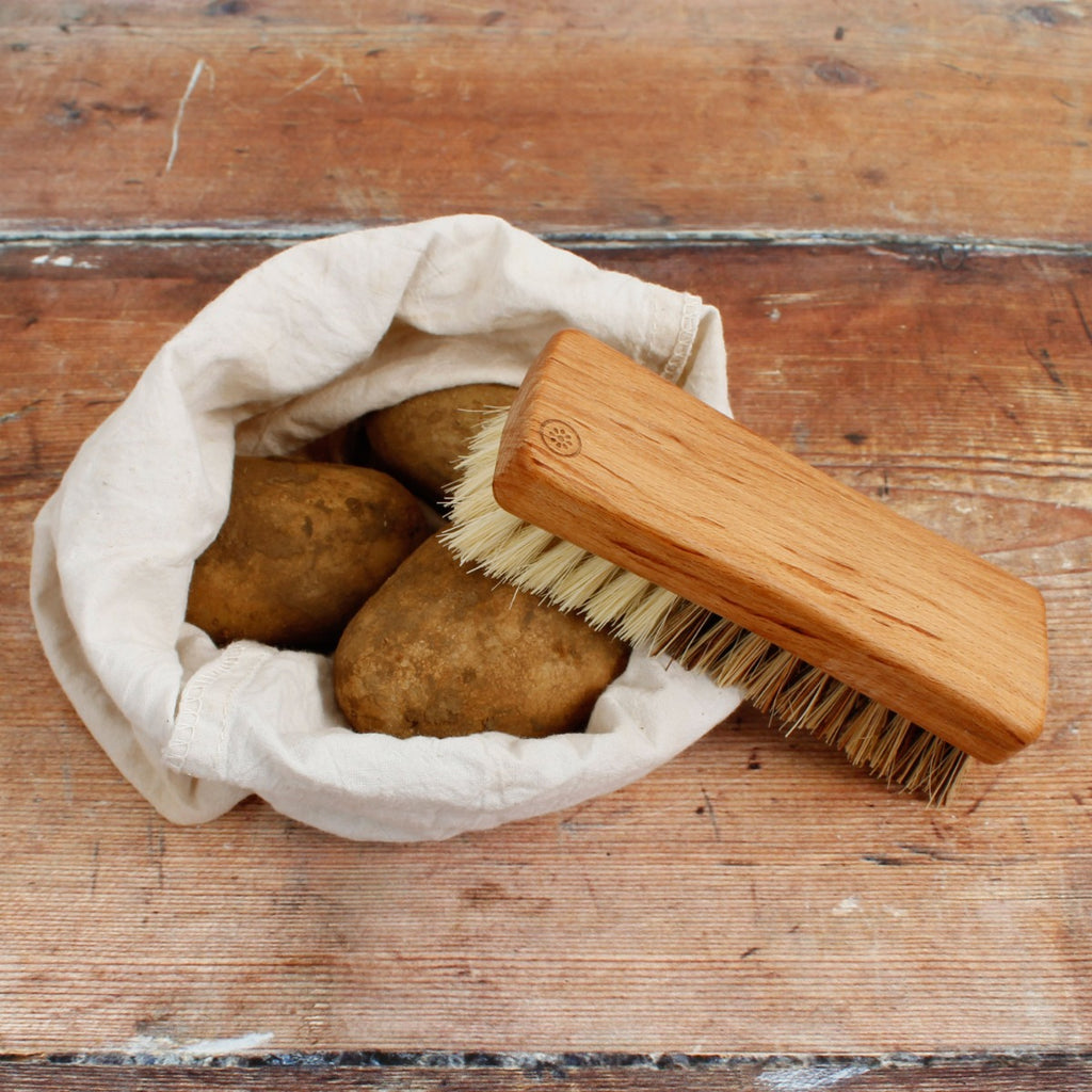 Wooden vegetable brush resting on a cloth bag of potatoes on a rustic wooden surface